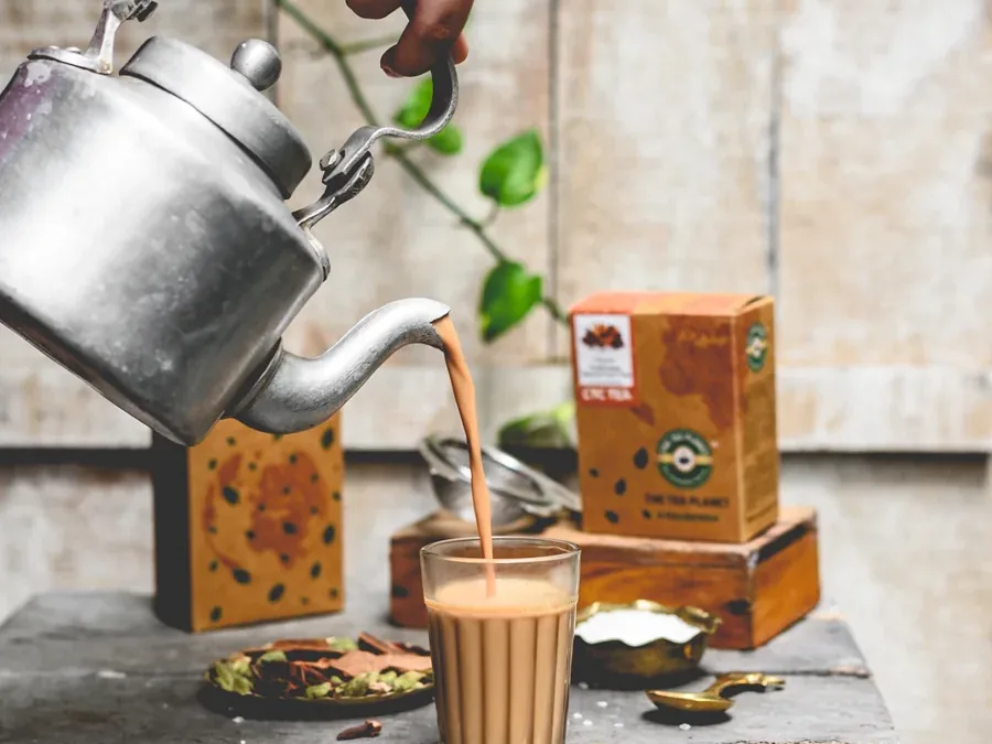 Masala chai poured from a kettle into a cutting-chai glass